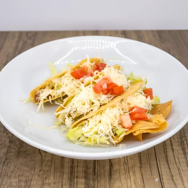Three crispy tacos filled with meat, lettuce, shredded cheese, and diced tomatoes on a white plate.