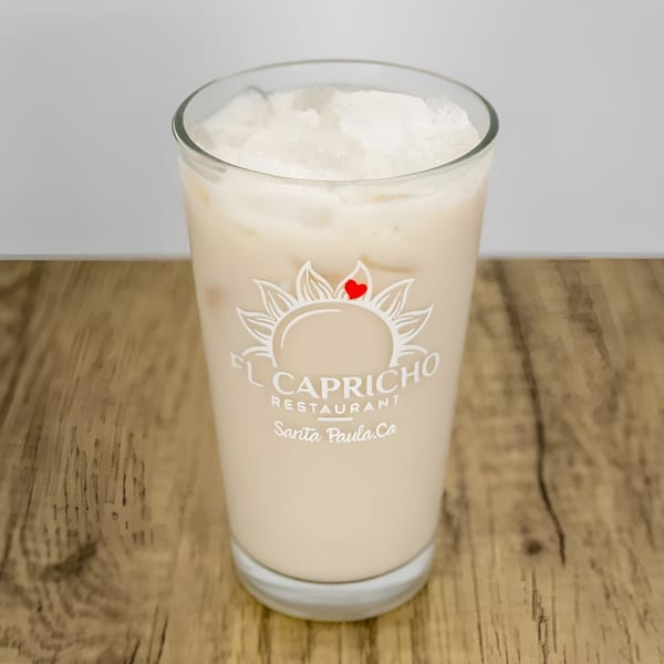 A glass of horchata with ice, featuring the El Capricho Restaurant logo, on a wooden table.
