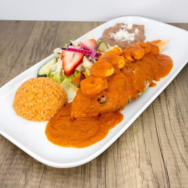 A Mexican dish with a whole fish covered in red sauce and shrimp, rice, beans, and salad.