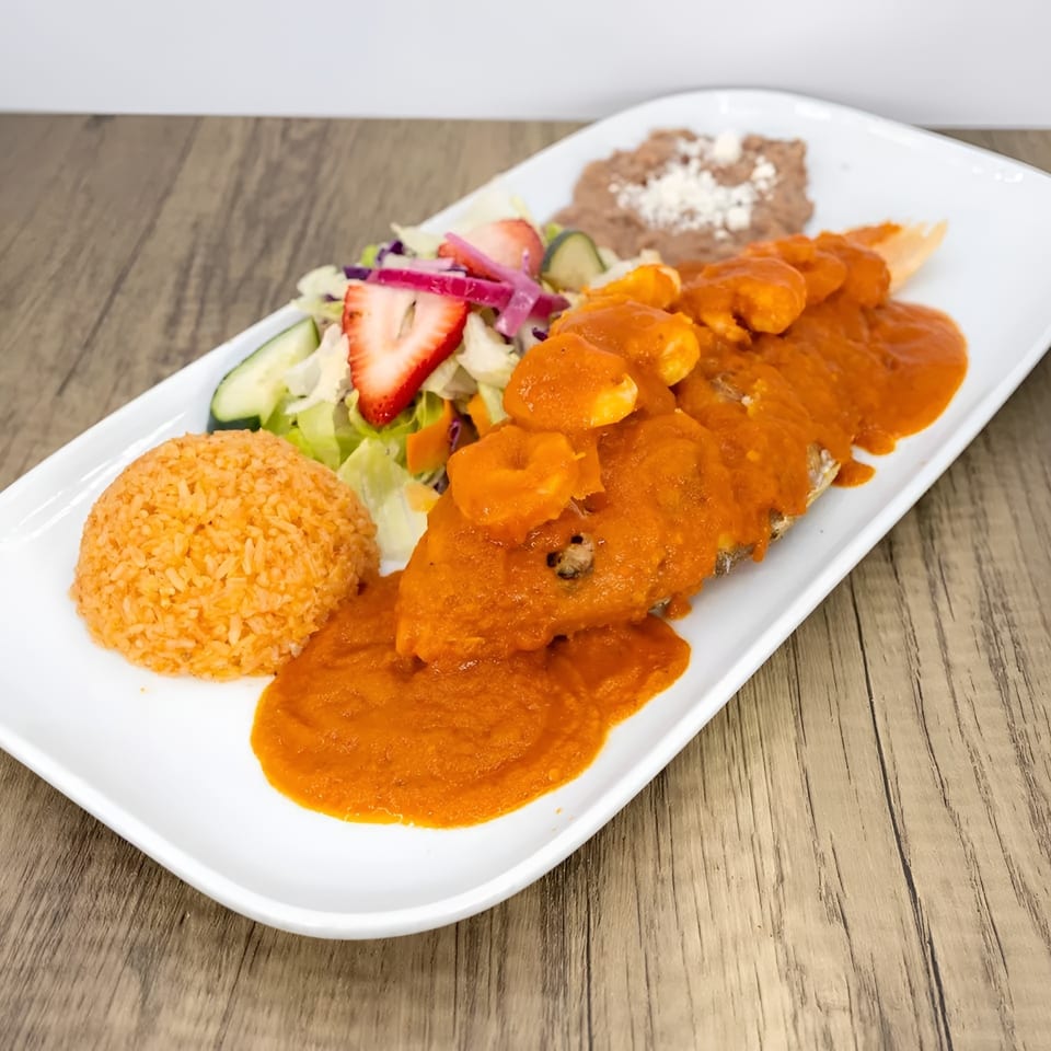 A Mexican dish with a whole fish covered in red sauce and shrimp, rice, beans, and salad.