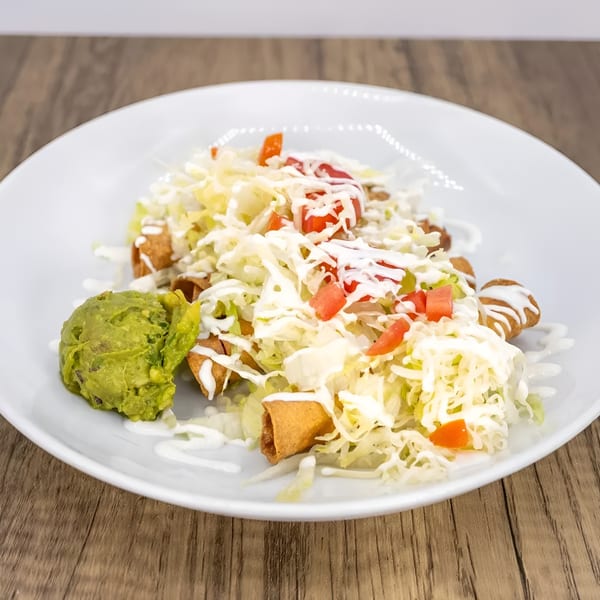 Taquitos topped with shredded lettuce, diced tomatoes, sour cream, and a side of guacamole.