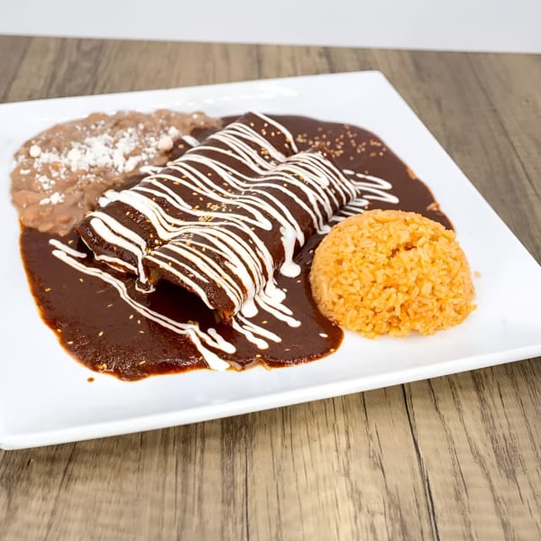 Three enchiladas covered in dark mole sauce with white crema, served with rice and refried beans.